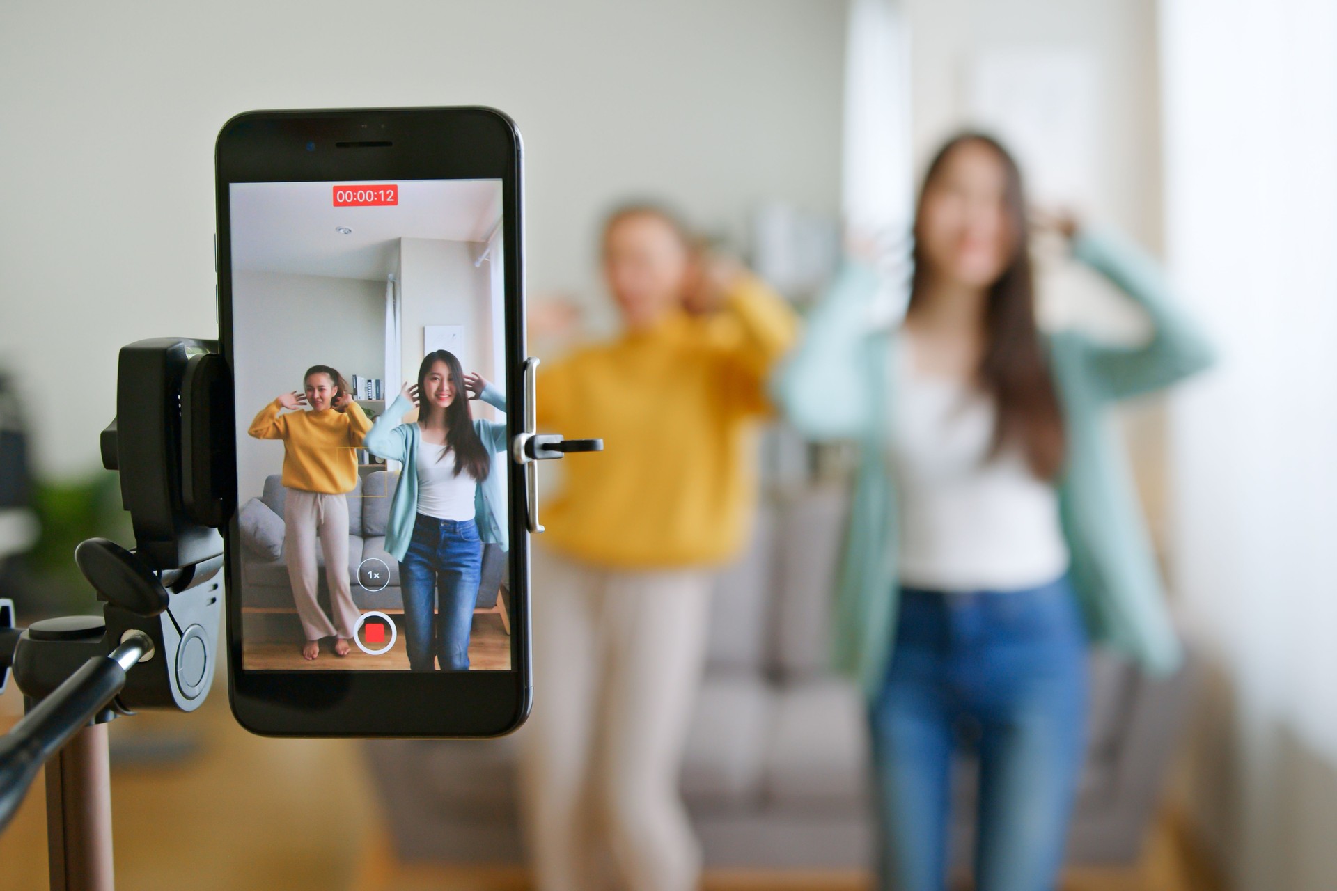 Asian young woman with her friend tiktoker created her dancing video by smartphone camera together. To share video to social media application